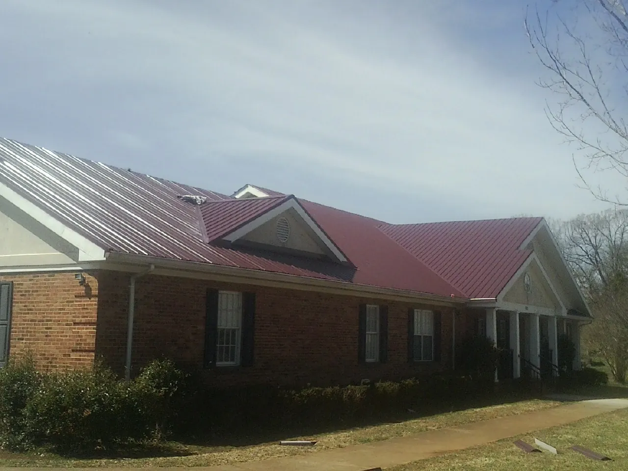 Red metal roof with gabled entries on a long brick building, from a Hail Damage Roof Repair job in Parksville